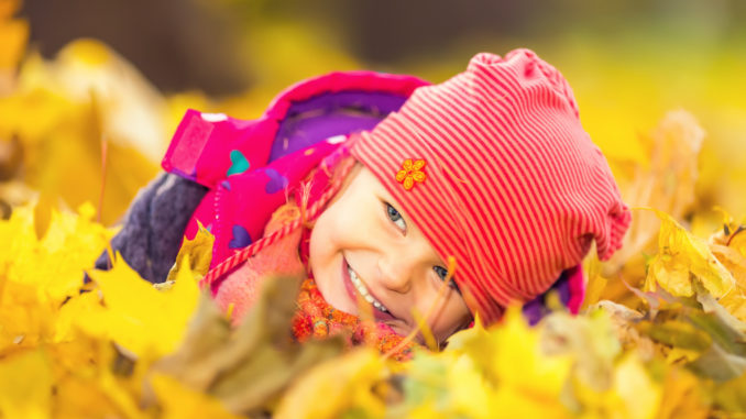 Little girl playing with autumn leaves