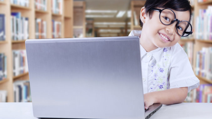 Adorable child sits in library with laptop